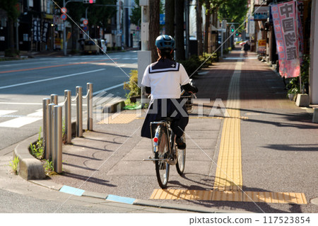 A high school girl wearing a helmet and cycling to school 117523854