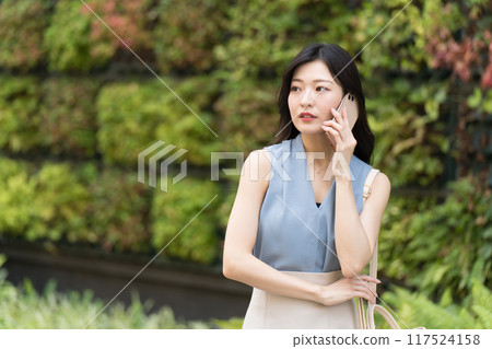 A businesswoman making a phone call on her smartphone in front of a building with green walls A businesswoman making a phone call on her smartphone in front of a building with green walls 117524158