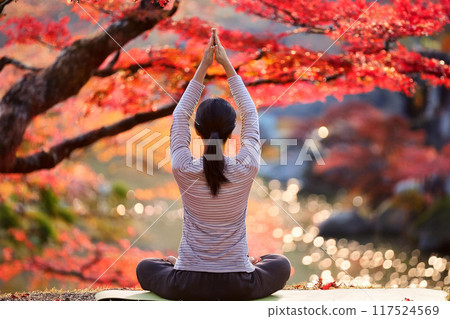 Back view of a young woman doing yoga with autumn scenery in the background 117524569