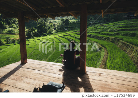 A man plays a guitar on the balcony of a house with a view of rice terraces. 117524699