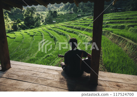 A man plays a guitar on the balcony of a house with a view of rice terraces. A man plays a guitar on the balcony of a house with a view of rice terraces. 117524700