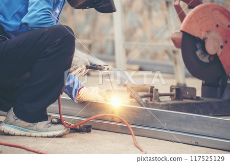 Construction Worker hands using Welding machinery iron metal sparking. Men hands wear protective glove Hot flame metal work cutting fire iron workshop. Locksmith use Welding machine cut metal process 117525129