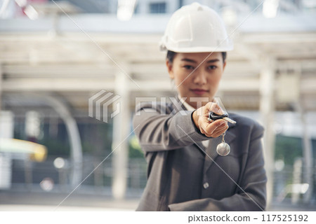 Civil women engineer wear safety white hard hat Hands using remote control car key. Close up hands of young woman showing key of new car. Businesswoman holding car rental key vehicle dealership. 117525192