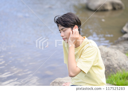 Young man cooling off by the water in summer and listening to music 117525283