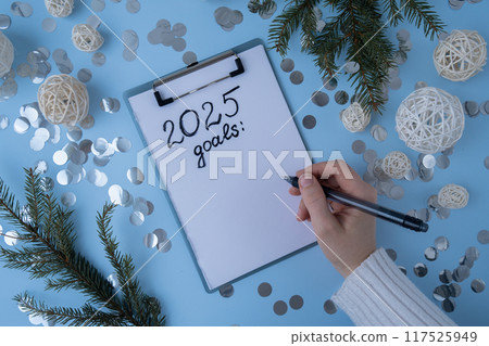 Female hands writing handwritten 2025 GOALS new year resolutions aims goals on paper notepad. Preparation for New Year. Planning and setting goals for personal development Female hands writing handwritten 2025 GOALS new year resolutions aims goals on paper notepad. Preparation for New Year. Planning and setting goals for personal development 117525949