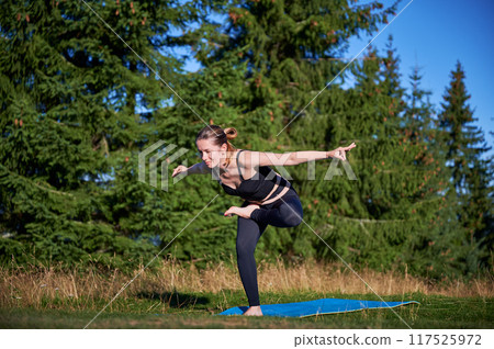 Woman practicing yoga outdoors in the mountains in a serene, natural setting. Female performing yoga pose on mat, with backdrop of beautiful mountain landscape at sunrise or sunset. 117525972