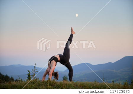 Woman practicing yoga outdoors in the mountains in a serene, natural setting. Female performing yoga pose, with backdrop of beautiful mountain landscape at sunrise or sunset. Woman practicing yoga outdoors in the mountains in a serene, natural setting. Female performing yoga pose, with backdrop of beautiful mountain landscape at sunrise or sunset. 117525975