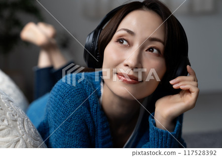 Middle-aged woman lying on the sofa listening to music Middle-aged woman lying on the sofa listening to music 117528392