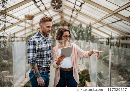 Small greenhouse business. Businesswoman and manager talking, standing in greenhouse, looking at camera, smiling. Small greenhouse business. Businesswoman and manager talking, standing in greenhouse, looking at camera, smiling. 117529857