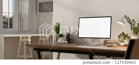Home workspace features a computer mockup on a wooden table in a contemporary bright room. 117530403