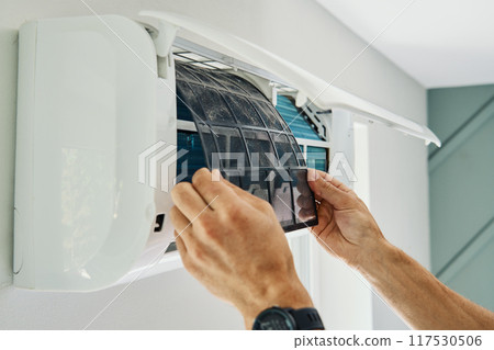 Air conditioner maintenance. Male technician repairs home climate system in living room. Man is cleaning filters of conditioner 117530506