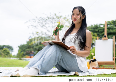 A beautiful Asian woman sitting on a picnic blanket in a park, posing and smiling at the camera. A beautiful Asian woman sitting on a picnic blanket in a park, posing and smiling at the camera. 117531198