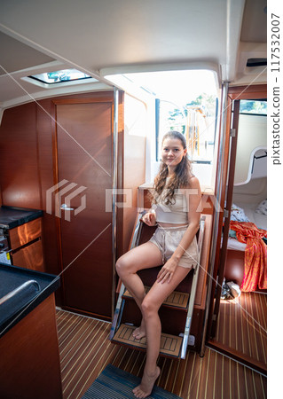 Young woman sits on the steps leading from the cockpit to the cabin of a yacht during sailing in sea. Yacht life concept 117532007