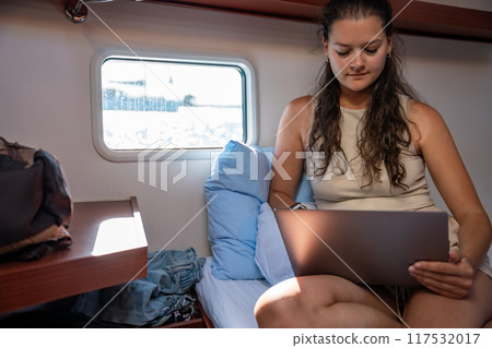 Young woman freelancer using laptop near window in the cabin of a yacht during sailing in sea. Yacht life concept Young woman freelancer using laptop near window in the cabin of a yacht during sailing in sea. Yacht life concept 117532017