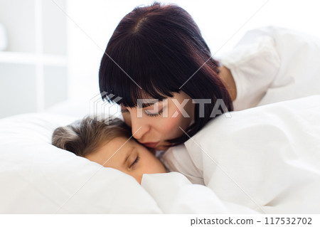 Mother kissing child goodnight in cozy bedroom 117532702