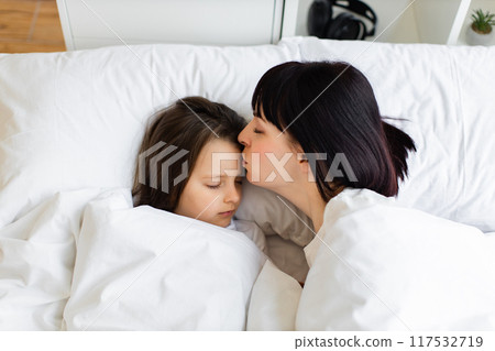 Mother kissing her sleeping child in bed during the morning 117532719