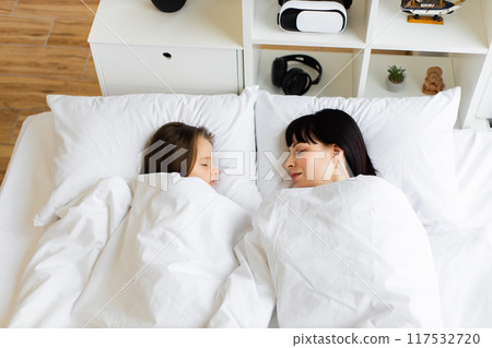 Mother and daughter sleeping peacefully in white bedroom 117532720