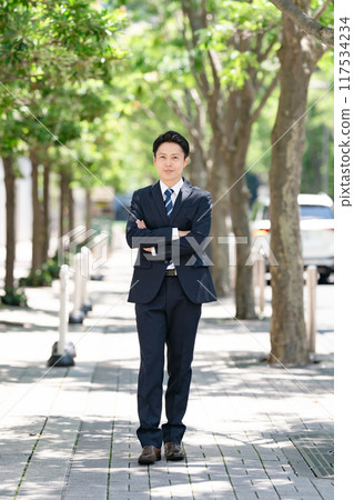 Businessman standing on a tree-lined street Businessman standing on a tree-lined street 117534234