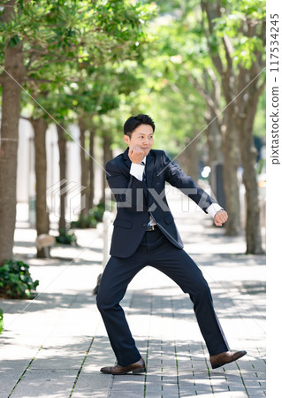 Businessman standing on a tree-lined street shadowboxing 117534245