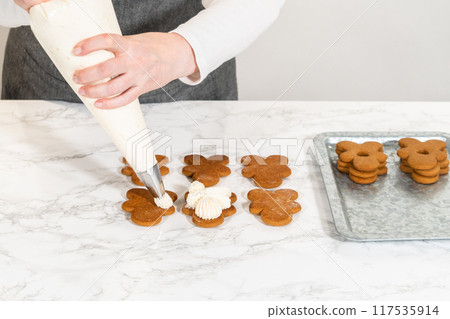 Gingerbread cookies await their second halves on a marble surface, each meticulously piped with buttercream to craft delightful sandwich treats. The precision of the piping adds a festive touch. Gingerbread cookies await their second halves on a marble surface, each meticulously piped with buttercream to craft delightful sandwich treats. The precision of the piping adds a festive touch. 117535914