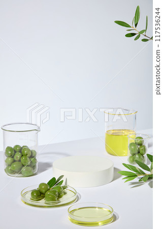 In the center is an empty pedestal in round shape for cosmetic product made from olive oil, surrounded by plenty glassware containing fresh olive and yellow olive oil. Photo from high angle shot In the center is an empty pedestal in round shape for cosmetic product made from olive oil, surrounded by plenty glassware containing fresh olive and yellow olive oil. Photo from high angle shot 117536244