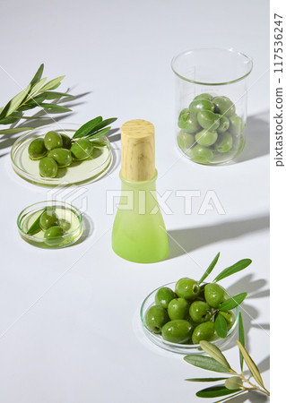 Olive oil-based cosmetic promotional photo was taken from above view on white table, with some glassware contain green olive displayed above. Mock up for promotional, space for text Olive oil-based cosmetic promotional photo was taken from above view on white table, with some glassware contain green olive displayed above. Mock up for promotional, space for text 117536247