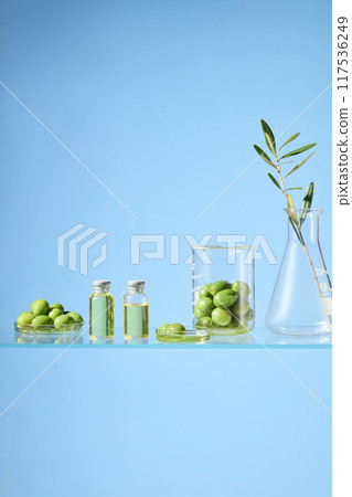 Olive in laboratory concept, fresh olive and olive oil contained in experiment glassware with some olive branch decorative, against on blue background. Blank space for designing, front view Olive in laboratory concept, fresh olive and olive oil contained in experiment glassware with some olive branch decorative, against on blue background. Blank space for designing, front view 117536249