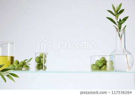 The photo of laboratory layout with fresh olive ingredient for beauty care product advertising, was taken from front view over white background. Space in center for product displaying, copy space 117536264