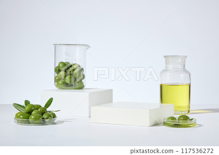 Olive cosmetic advertising template from front view, on white background. Empty pedestal for product displaying, surrounded with glass bottle, beaker and petri dish contains green olive and olive oil Olive cosmetic advertising template from front view, on white background. Empty pedestal for product displaying, surrounded with glass bottle, beaker and petri dish contains green olive and olive oil 117536272