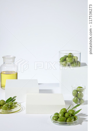 High angle shot photo on white background with some empty podiums for natural cosmetic displaying, dotted with green color of fresh olives and yellow olive oil. Copy space for text High angle shot photo on white background with some empty podiums for natural cosmetic displaying, dotted with green color of fresh olives and yellow olive oil. Copy space for text 117536273