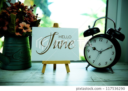 Hello June text on paper card with easel and alarm clock in the window background 117536290