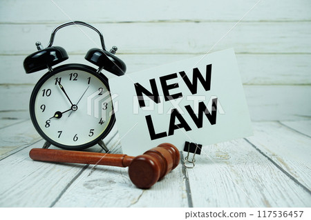 New Law text on paper card with alarm clock and wooden judge gavel on wooden background New Law text on paper card with alarm clock and wooden judge gavel on wooden background 117536457