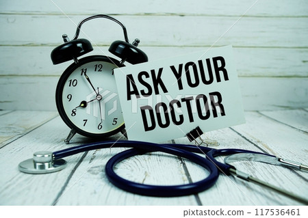 Ask Your Doctor text on paper card with alarm clock and stethoscope on wooden background 117536461