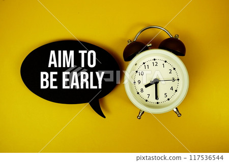 Aim To Be Early text on speech bubble with alarm clock top view on yellow background 117536544
