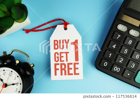 Top view of Buy One Get One Free text on tag sale with calculator and black alarm clock flat lay on blue background 117536814