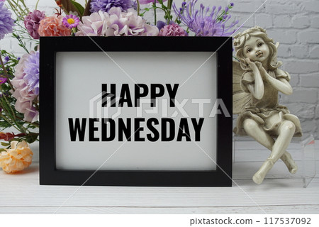 Happy Wednesday text with flowers and ceramic doll decoration on white brick wall and wooden background 117537092