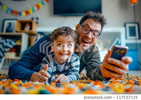 A man and a boy are laying on the floor, playing with a cell phone 117537135