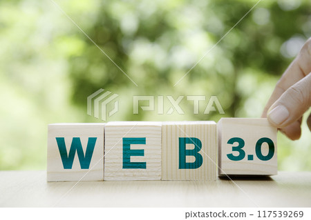 Web 3.0 icon in wood on green background. Businessman hand turns cubes and changes the word web 3.0.Technology and WEB 3.0 concept. Web 3.0 icon in wood on green background. Businessman hand turns cubes and changes the word web 3.0.Technology and WEB 3.0 concept. 117539269