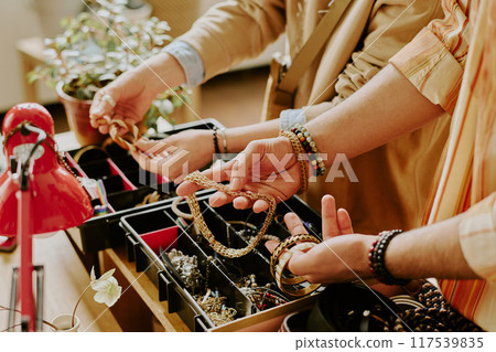 Close-up of hands choosing necklace and bracelets from display in jewelry shop showing intricate details and accessories being examined and selected with care Close-up of hands choosing necklace and bracelets from display in jewelry shop showing intricate details and accessories being examined and selected with care 117539835