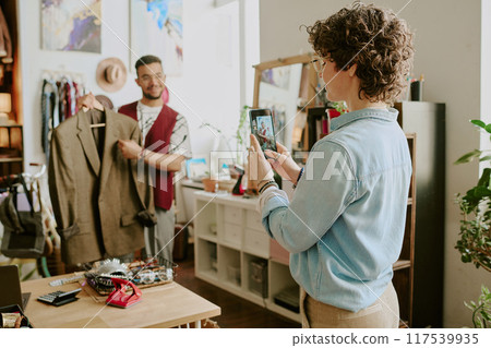 Two colleagues reviewing business attire in office setting. One holding jacket while other using tablet for documentation while engaging in discussion Two colleagues reviewing business attire in office setting. One holding jacket while other using tablet for documentation while engaging in discussion 117539935