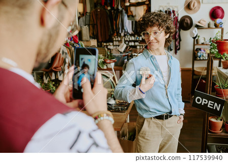 Woman with curly hair smiling while holding handmade item in artisan shop filled with various crafted goods 117539940