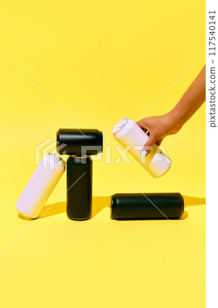 Minimalistic mockup with black and white cans on yellow background, with hand picking up one can. Beer, lemonade, soda water, energy drinks packaging. Minimalistic mockup with black and white cans on yellow background, with hand picking up one can. Beer, lemonade, soda water, energy drinks packaging. 117540141