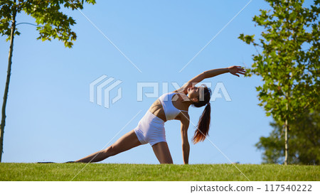 Embracing nature's calm, woman flows into side stretch, perfect blend of strength and flexibility in peaceful yoga moment. 117540222