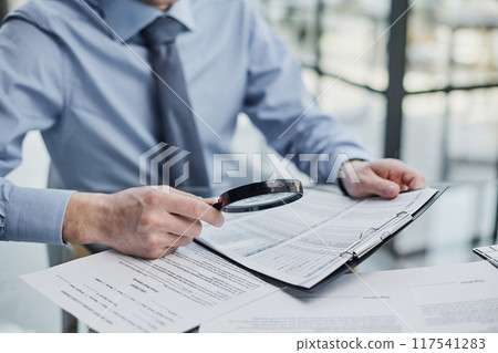Businessman looking through a magnifying glass to documents Businessman looking through a magnifying glass to documents 117541283