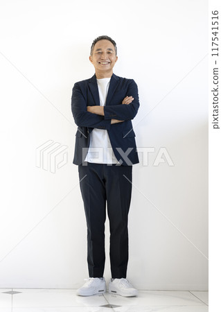 A man in his early 60s smiling at the camera with his arms folded, full body 117541516