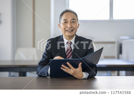 A businessman in his 60s looking at the camera while talking and holding a file 117541588