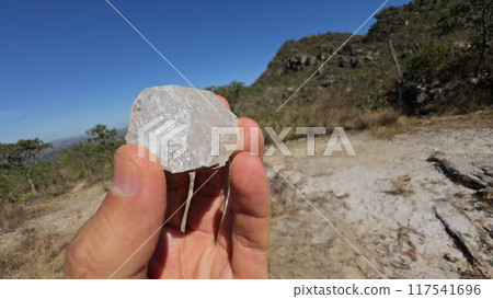 Hand examining a white semi-transparent stone near outdoors 117541696