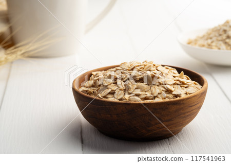 Oat flakes or rolled oats in wooden bowl on white plate.healthy eating, vegan food. Oat flakes or rolled oats in wooden bowl on white plate.healthy eating, vegan food. 117541963