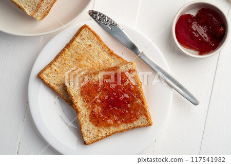 Close up Toast bread and Strawberry Jam.Spreading jam on slice whole wheat bread in white plate. Close up Toast bread and Strawberry Jam.Spreading jam on slice whole wheat bread in white plate. 117541982