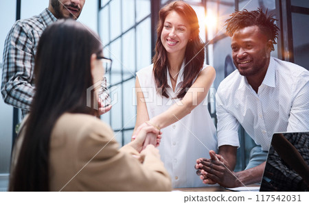 Diverse group of coworkers listening to a presentation during a staff meeting around a table in an office 117542031